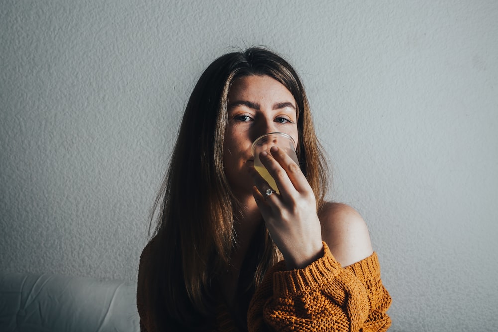 a woman in an orange sweater drinking from a glass