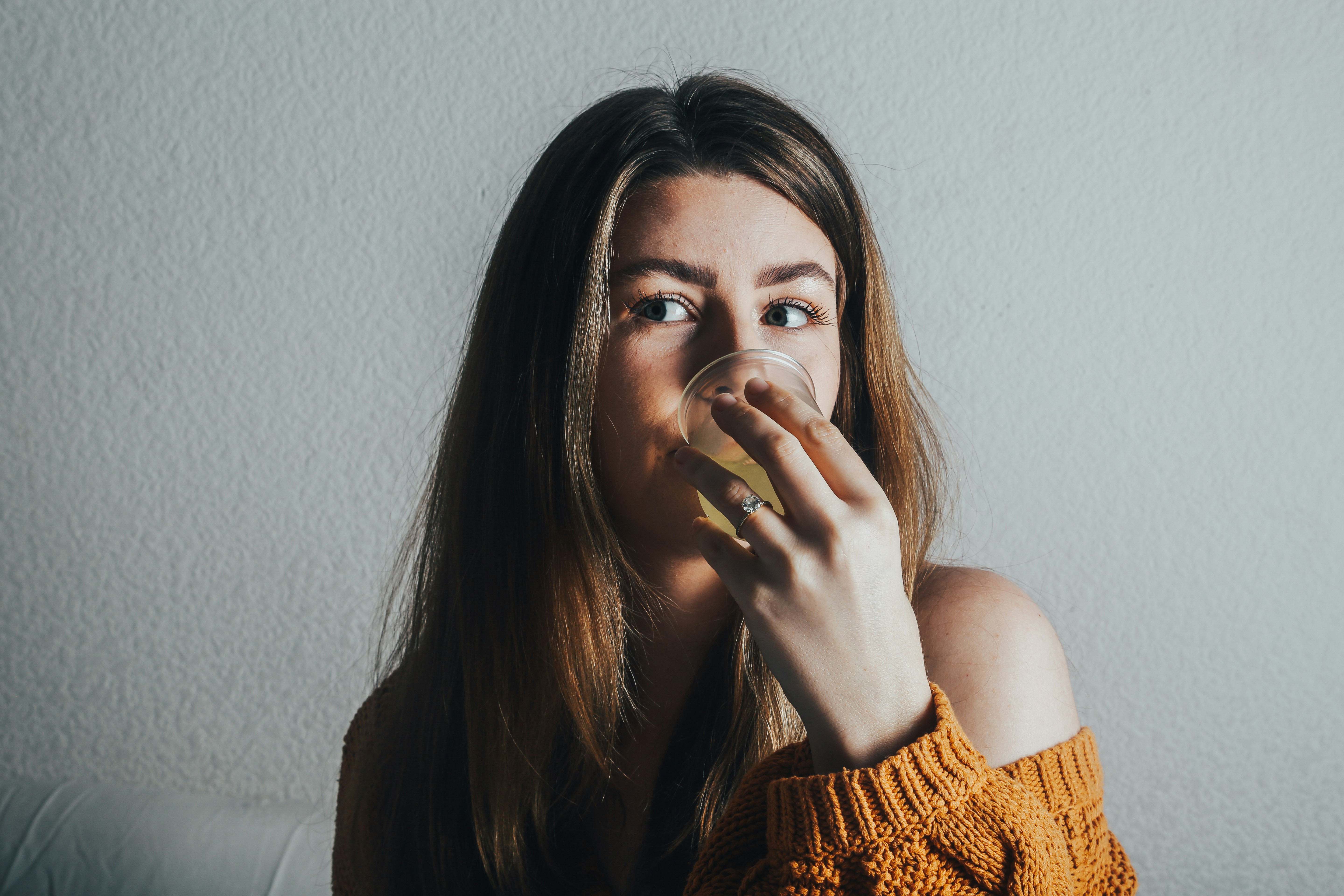 a woman in an orange sweater drinking from a glass
