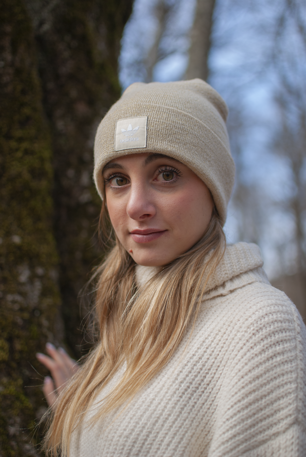 a woman wearing a beanie standing next to a tree