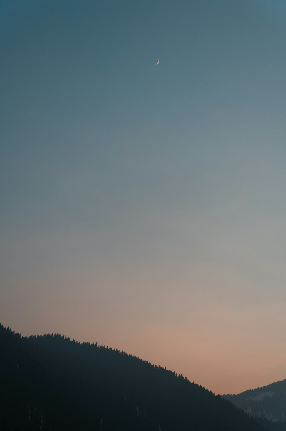 a view of a mountain with a moon in the sky