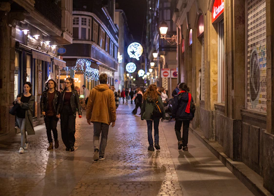 A lively street scene in Reims at night with people using their smartphones.