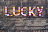 Colorful LEGO bricks are arranged to spell the word 'LUCKY' against a dark wooden background with visible grain patterns.