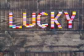 Colorful LEGO bricks are arranged to spell the word 'LUCKY' against a dark wooden background with visible grain patterns.