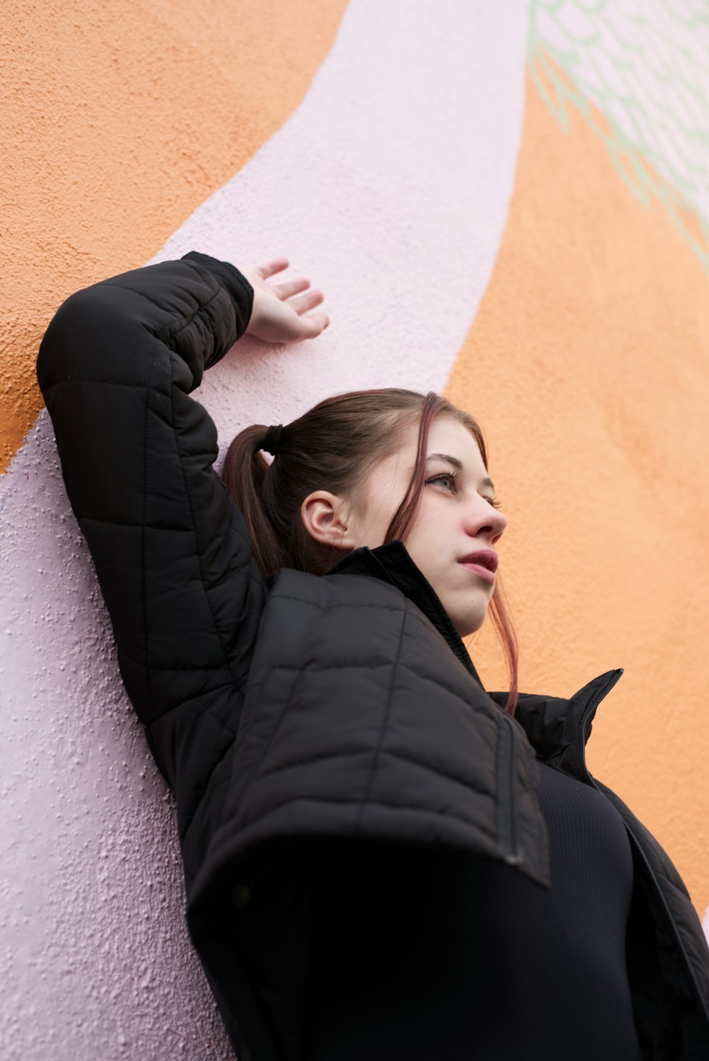 a woman leaning against a wall wearing a black jacket
