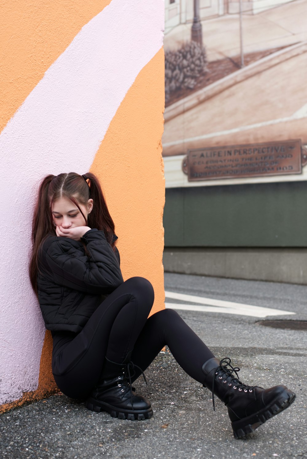 a woman sitting against a wall talking on a cell phone
