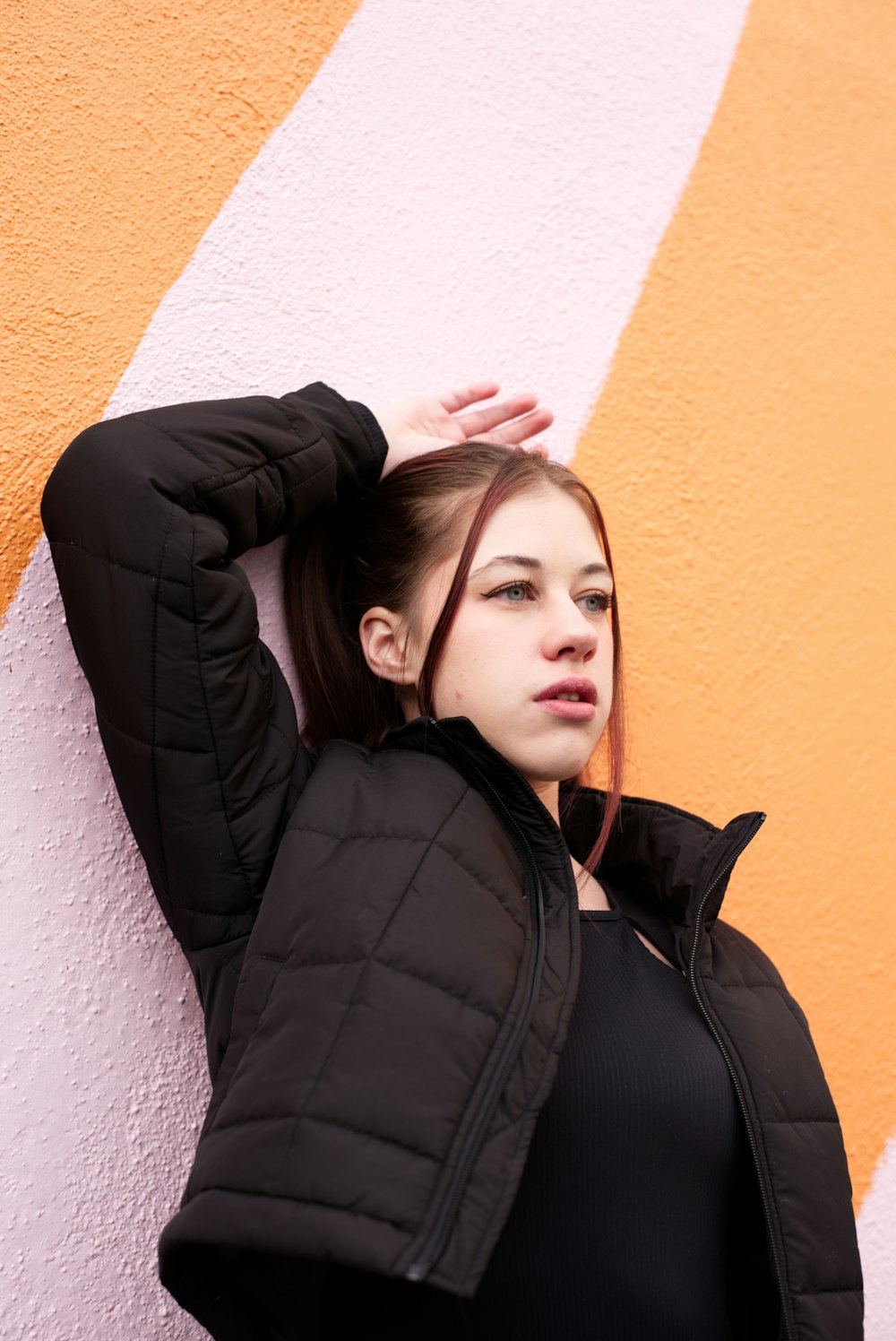 a woman in a black jacket leaning against a wall