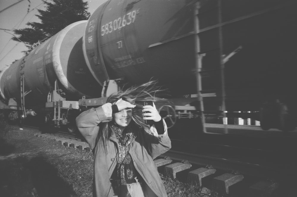 a black and white photo of a woman taking a picture of a train