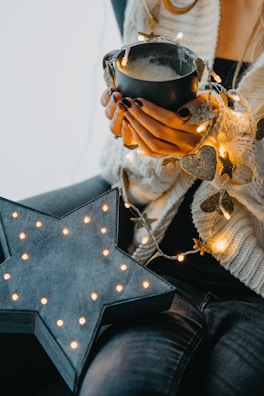 A person wrapped in a warm blanket holding a mug of sleepy-time tea, with a background of twinkling fairy lights.