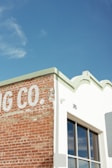 A corner of a building with a partially visible sign that reads 'G CO.' on a weathered brick wall, next to a white section with a large window reflecting the sky. The rooftop features decorative edges and the number 315 is visible.