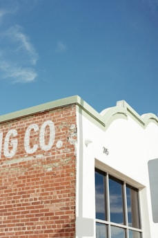 A corner of a building with a partially visible sign that reads 'G CO.' on a weathered brick wall, next to a white section with a large window reflecting the sky. The rooftop features decorative edges and the number 315 is visible.