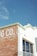 A corner of a building with a partially visible sign that reads 'G CO.' on a weathered brick wall, next to a white section with a large window reflecting the sky. The rooftop features decorative edges and the number 315 is visible.