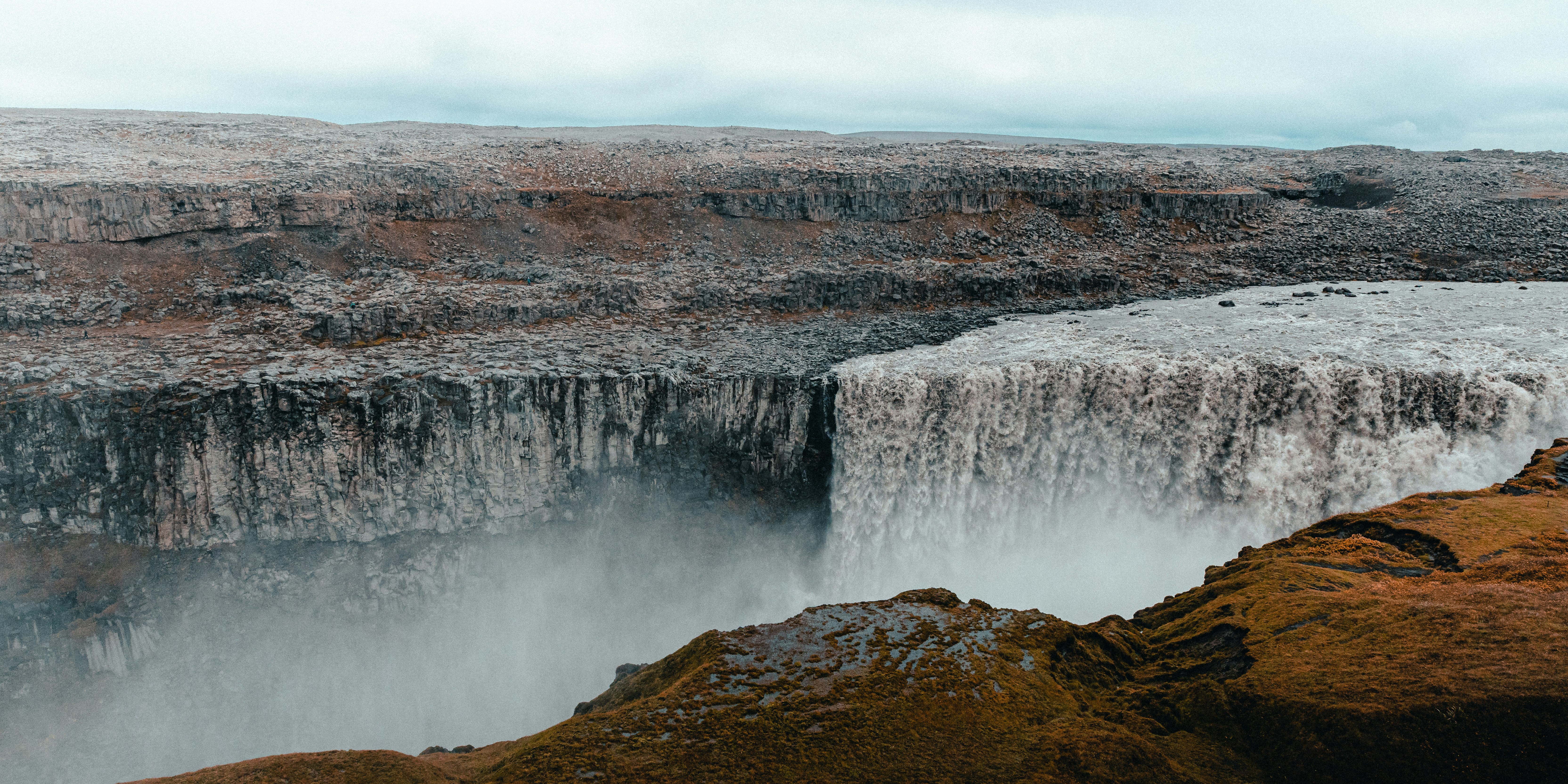 a man standing on the edge of a cliff next to a waterfall