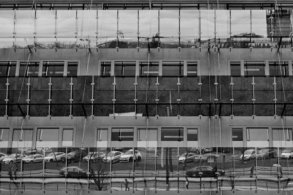 a black and white photo of a building with cars reflected in it