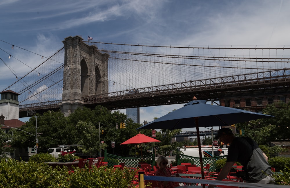 a man sitting under an umbrella in front of a bridge