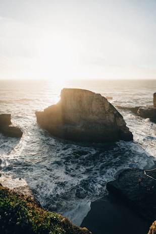 Rocky coastline with crashing waves and textured cliffs bathed in late afternoon light.