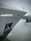 Close-up of a polished yacht bow gently rocking beside a modern marina pier.