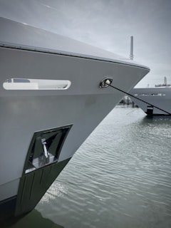 A close-up of a surveyor inspecting a ship's hull at a bustling port under clear skies.