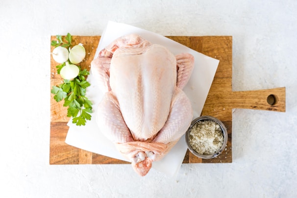 Fresh whole chicken on a rustic wooden cutting board with herbs around.