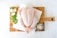 A raw whole chicken placed on a wooden cutting board, accompanied by fresh parsley, onions, and a small bowl of salt.