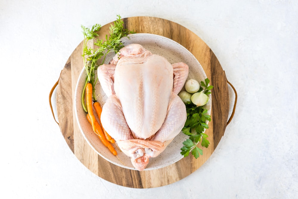 a raw chicken on a wooden platter with vegetables