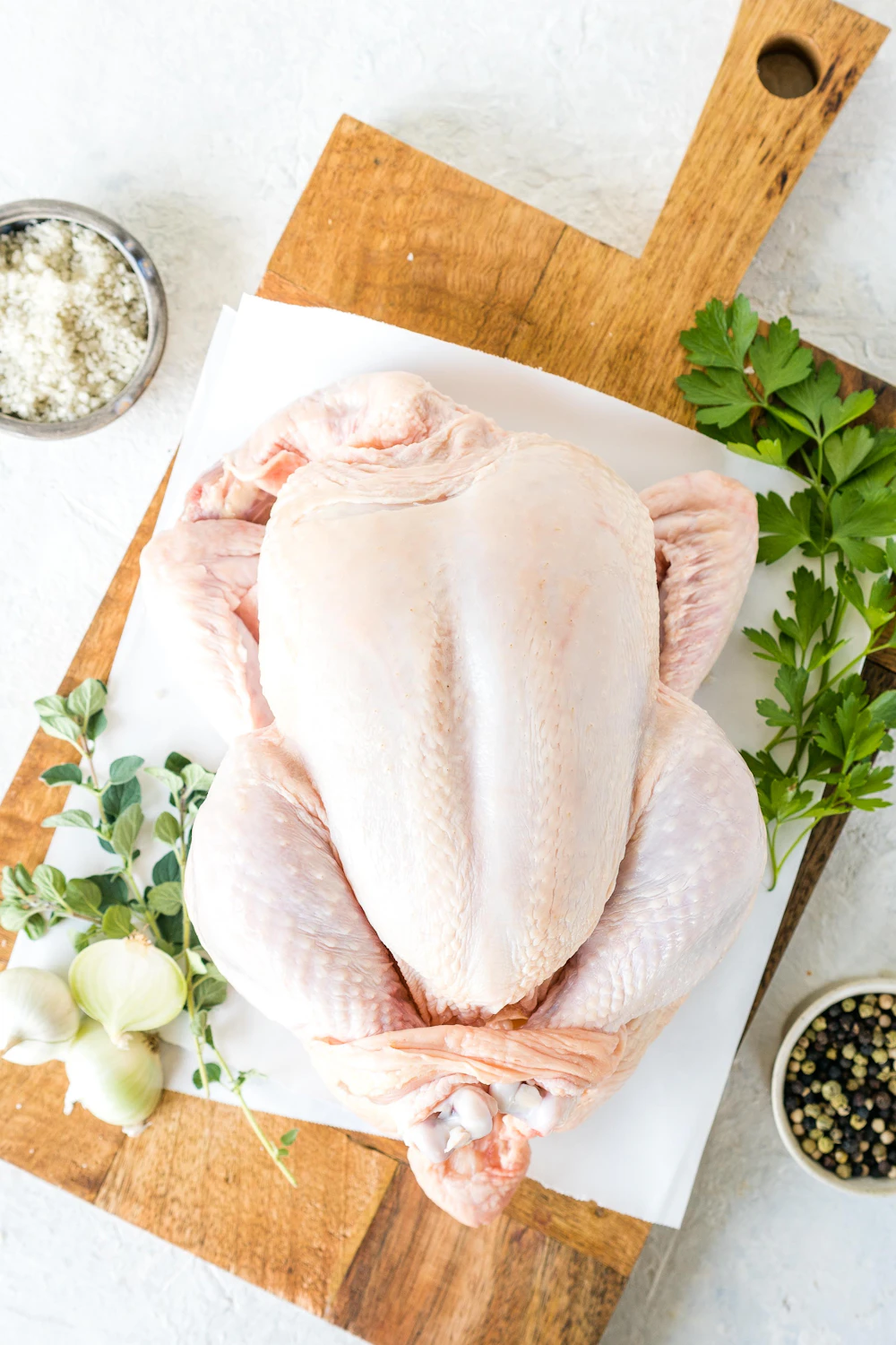 Whole dressed prime chicken on a wooden board with fresh herbs