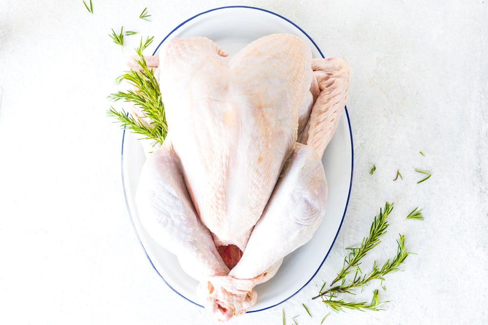 a whole chicken on a plate with a sprig of rosemary