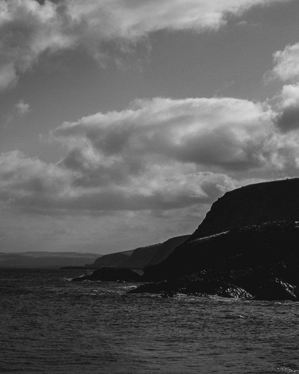 a black and white photo of a lighthouse on a cliff