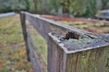 A close-up of a craftsman’s hands repairing a weathered fence post with new hardware.