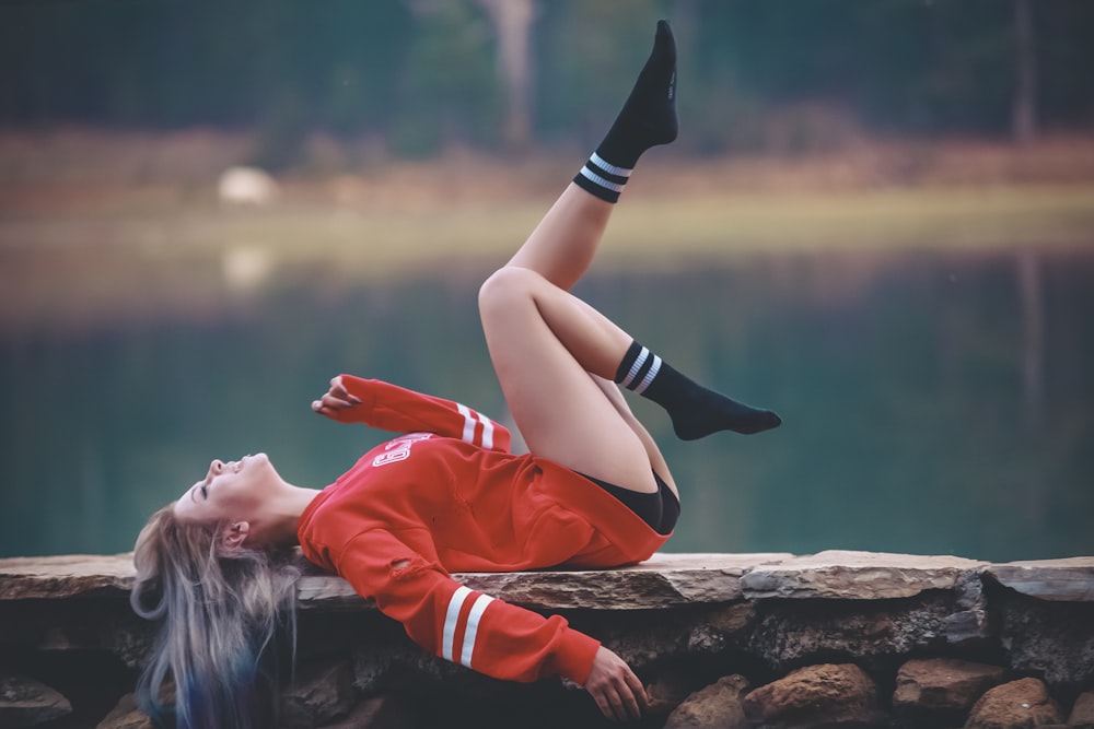 a woman laying on a stone wall next to a body of water