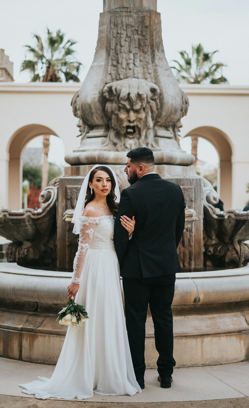 a bride and groom standing in front of a fountain