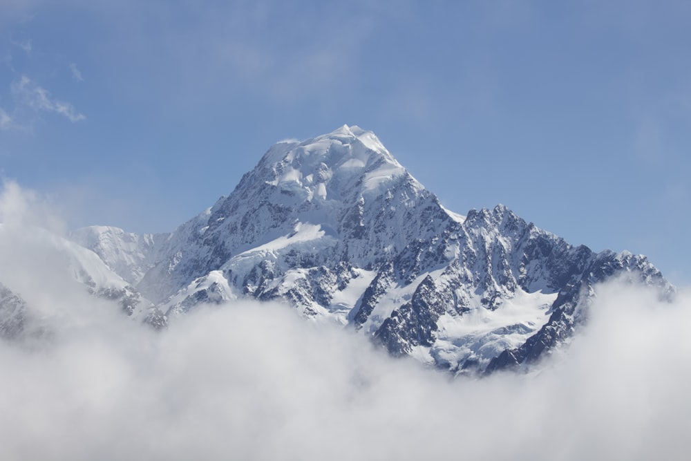 a mountain covered in snow and clouds under a blue sky