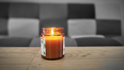 A softly lit candle in a sleek glass jar resting on a minimalist wooden table.