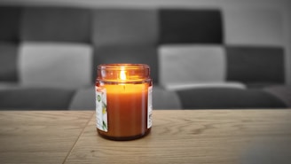 A beautifully lit classic scented jar candle with a smooth glass vessel on a wooden table.