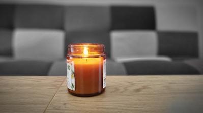 A beautifully lit classic scented jar candle with a smooth glass vessel on a wooden table.