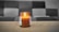 A softly glowing jar candle resting on a polished wooden table surrounded by cozy, decorative elements.