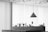 A monochrome image of an interior space featuring a modern hanging pendant light above a shelf or desk. Several small objects are neatly arranged along the surface, including bottles, vases with plants, and a sign. The ceiling has an array of circular cutouts, and the large windows in the background are covered with blinds or curtains, diffusing the light.
