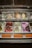 A variety of ice cream flavors displayed in metal containers inside a glass-topped freezer. Each flavor is labeled with circular tags, showing different colors and text. The ice creams include a mix of vibrant colors such as green, purple, and pink.