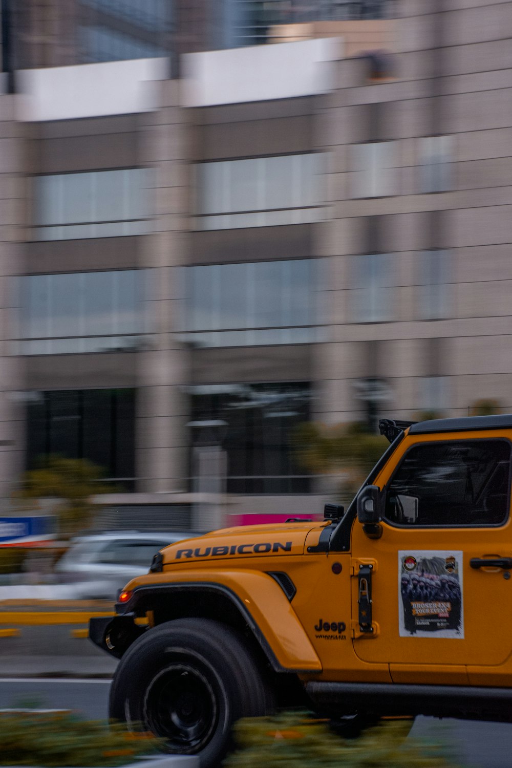 a yellow jeep driving down a street next to a tall building