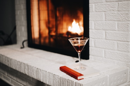 A cozy scene with a glass of whisky and a glowing fireplace in the background.