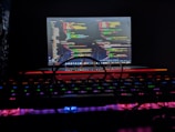 Close-up of hands typing code on a laptop with neon blue and purple reflections.