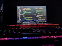 Close-up of modern hands typing code on a dark-themed laptop keyboard illuminated by green backlight.