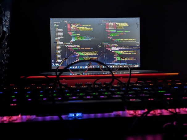 Close-up of hands coding on a laptop with neon purple and blue light reflections.