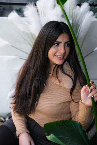 A soft-lit, airy photo of a woman in a cozy knit sweater surrounded by delicate greenery and natural light.