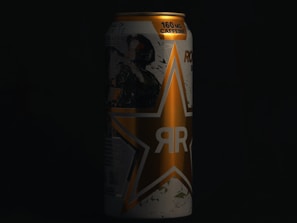 A can with a prominent star logo covers the main portion of the image. The can displays text indicating 160mg of caffeine along the top. The design style is bold, with a color scheme that includes gold and dark shades.