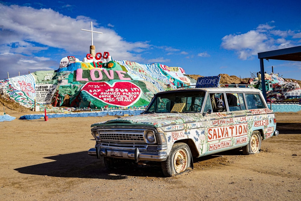 an old station wagon parked in front of a colorfully painted mountain