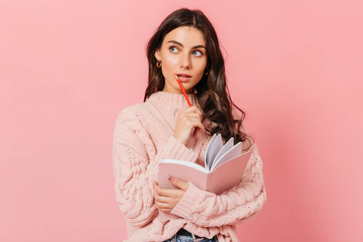 a woman in a pink sweater is holding a book and looking at the camera