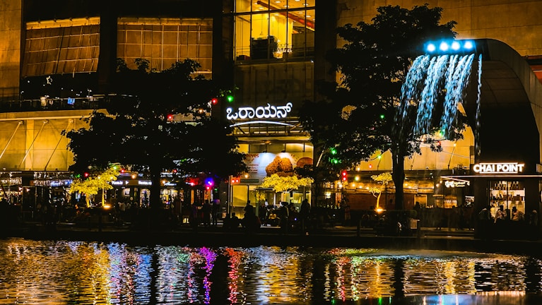 A vibrant city plaza bustling with diverse people and greenery under soft evening light.
