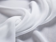 Soft, flowing white fabric creates delicate folds and curves, evoking a sense of smoothness and elegance.