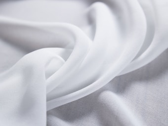 Soft, flowing white fabric creates delicate folds and curves, evoking a sense of smoothness and elegance.