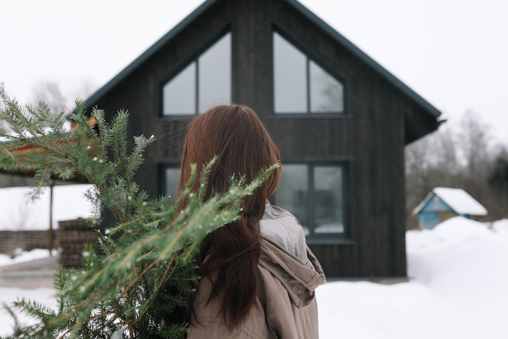 a woman standing in front of a house holding a christmas tree